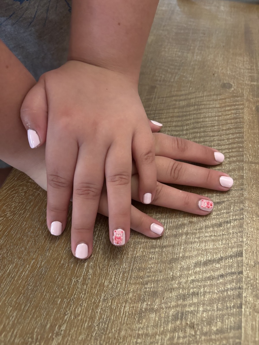 A child's soft-pink manicure with a tiny pink bear accent — kids' nails
