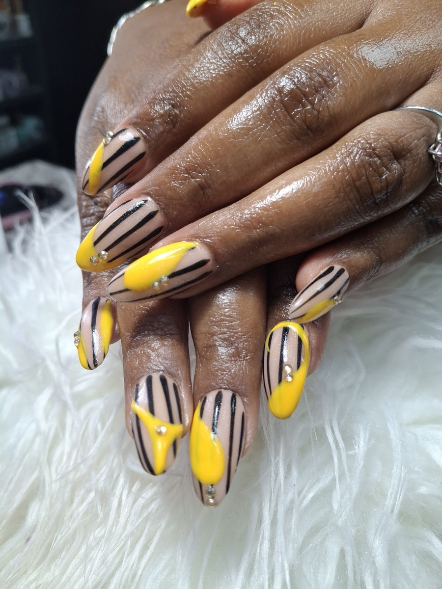 Nude stiletto nails with black pinstripes, yellow tips, and crystal detail